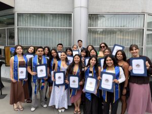 Students working with LPPI smile with Scrolls of Recognition from the California State Assembly. Many are wearing blue graduation stoles.